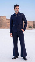 A man wearing a dark navy blue western-style jacket and matching flared trousers stands outdoors in a snowy landscape with sandstone fort walls in the background.
