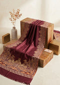 A deep maroon and gold patterned shawl draped over wooden display blocks in a warm, minimalist studio setting.