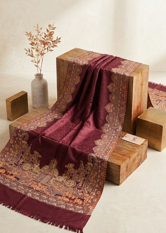A deep maroon and gold patterned shawl draped over wooden display blocks in a warm, minimalist studio setting.
